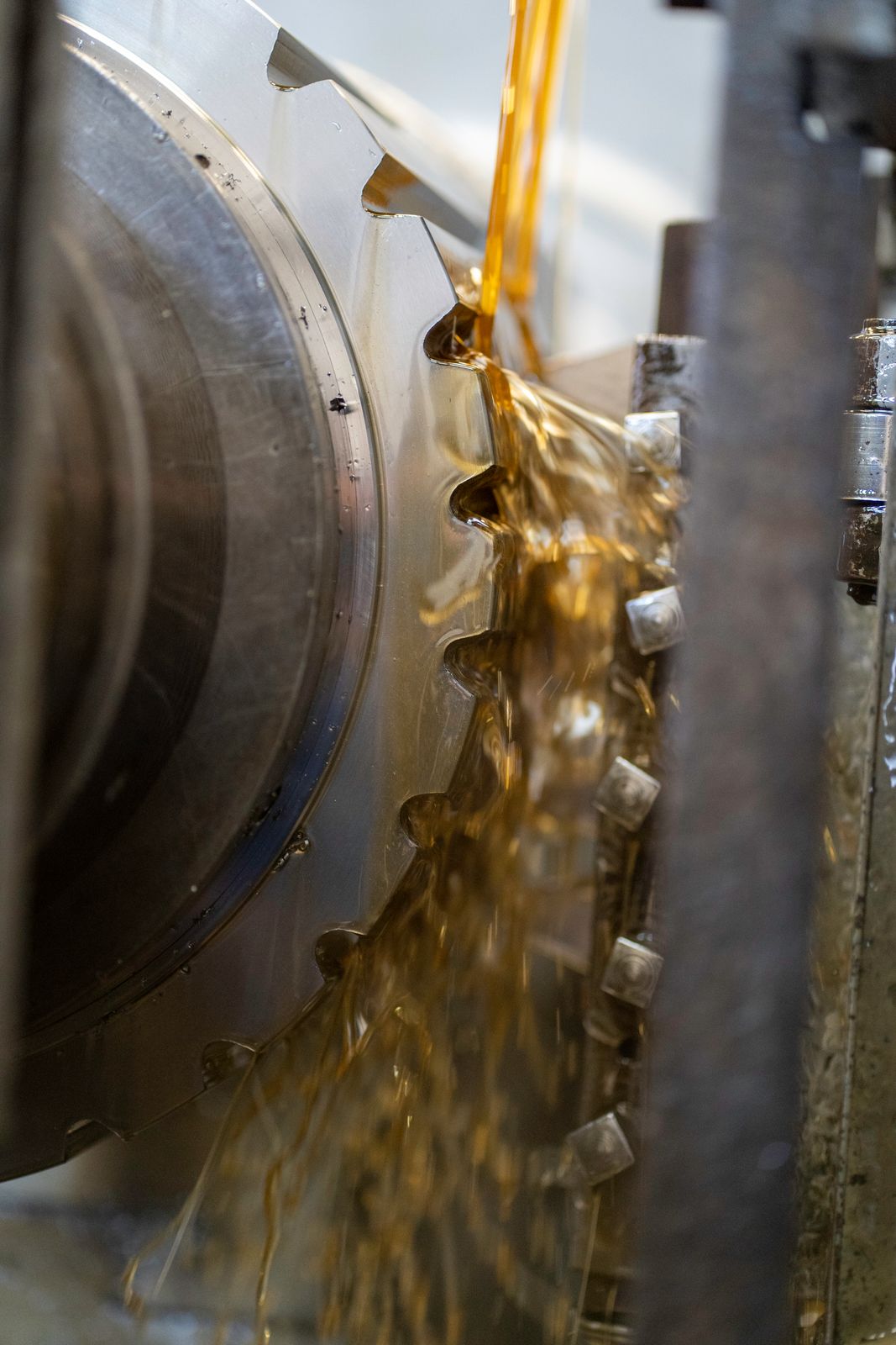 Close-up of golden fluid pouring onto the teeth of a large metal gear in a machine