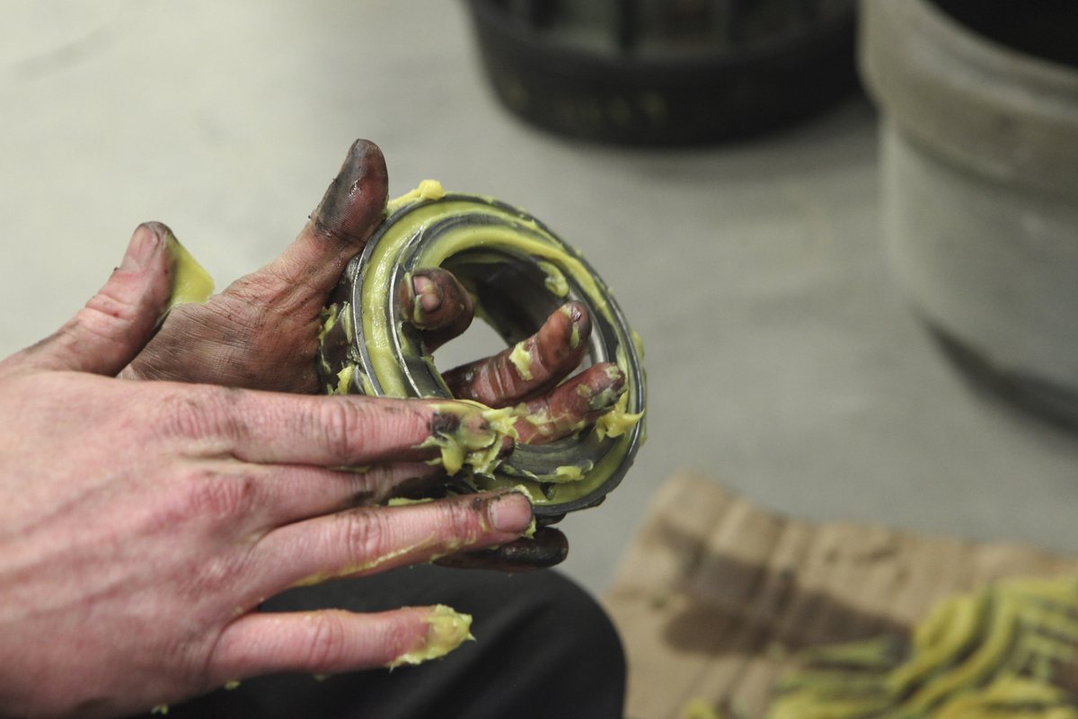 Grease-covered fingers packing yellow grease into a trailer bearing held in one hand.