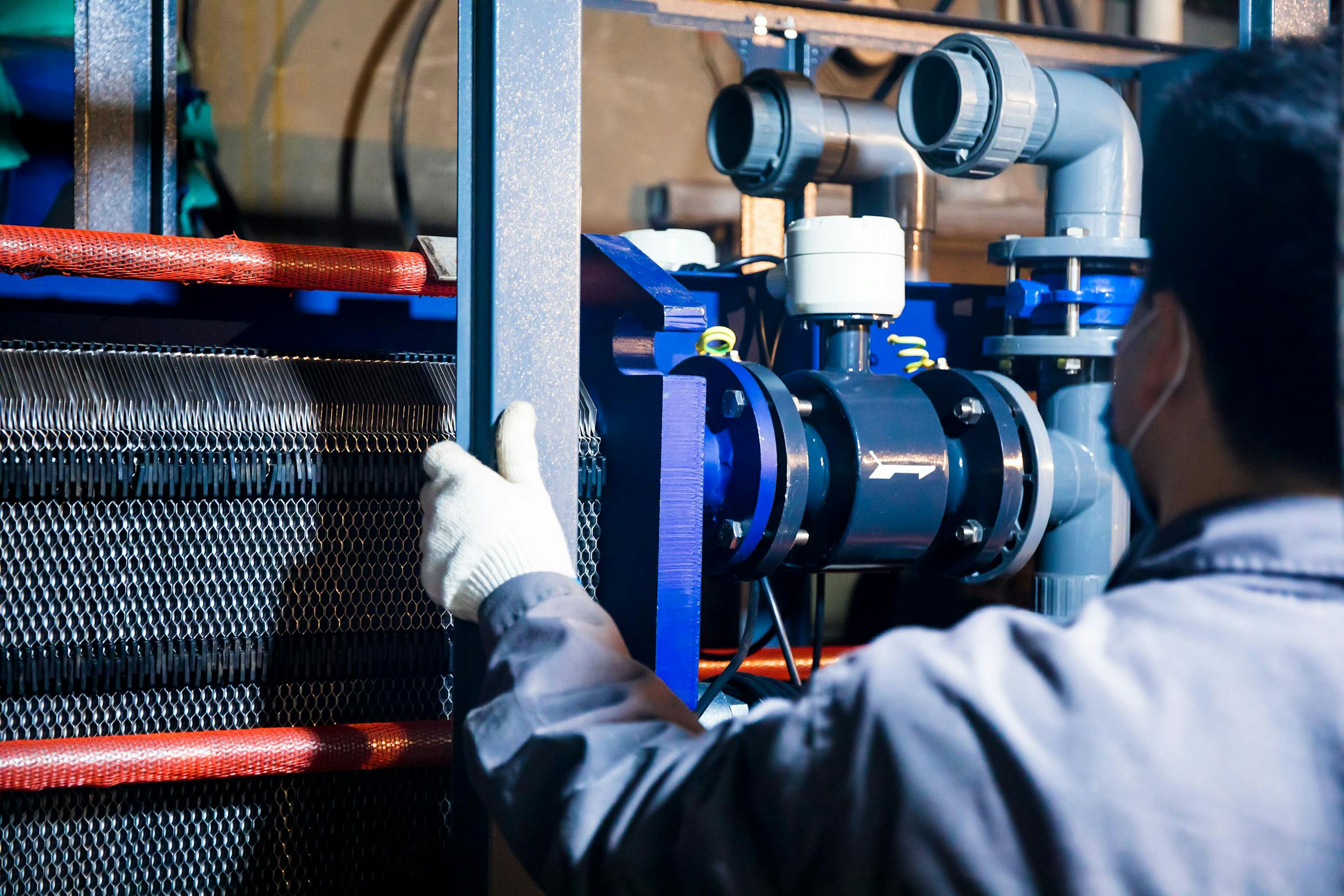 A worker beside industrial machinery and pipework.